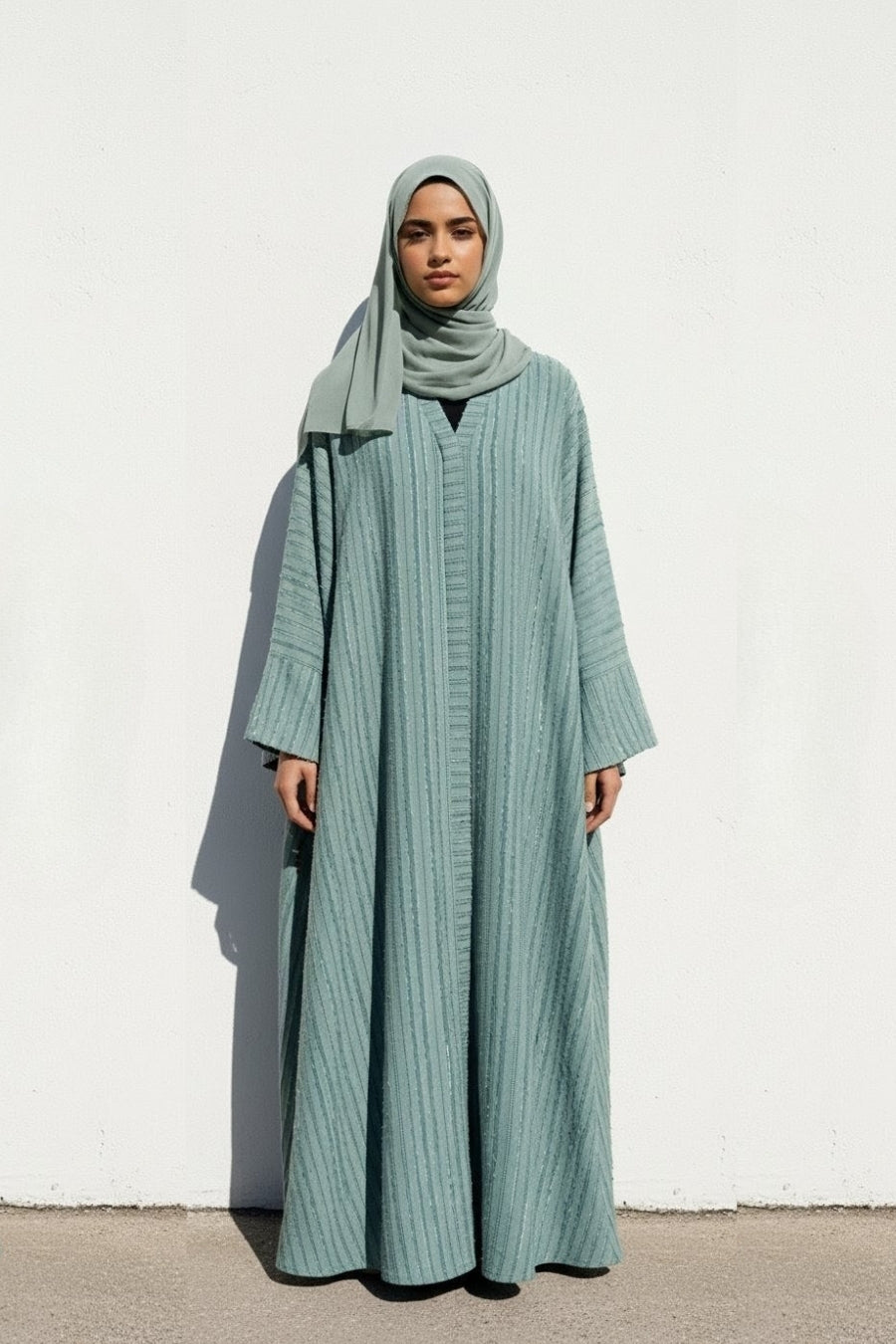 Woman wearing a long light blue abaya and hijab against a white background